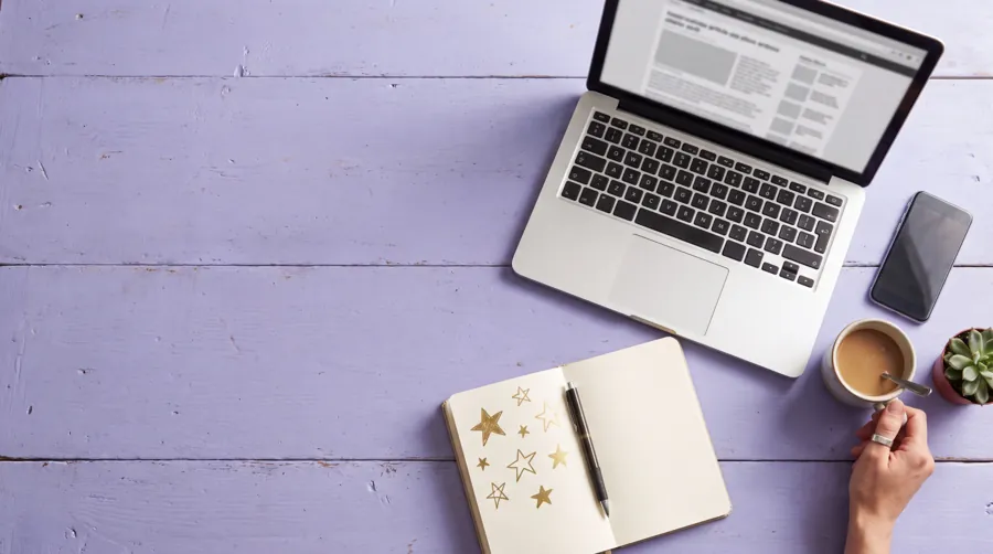 Overhead view of a lavender desk with laptop, phone, coffee and a notebook of gold star doodles